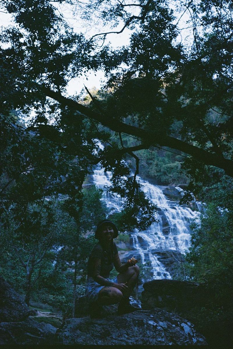 A waterfall dropping through dense green foliage, photographed upright, a figure standing at its base.