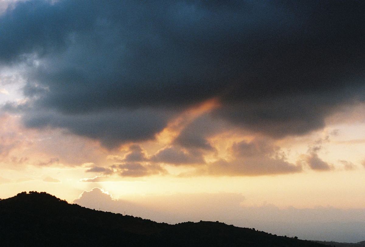 A ridge in silhouette under a wide sunset, heavy cloud breaking to a band of orange at the horizon.